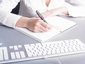 Woman sitting at desk with pen in hand writing, page is blank